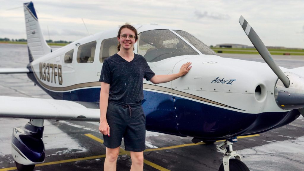 Kobi Hamby stands in front of a small propellor airplane.