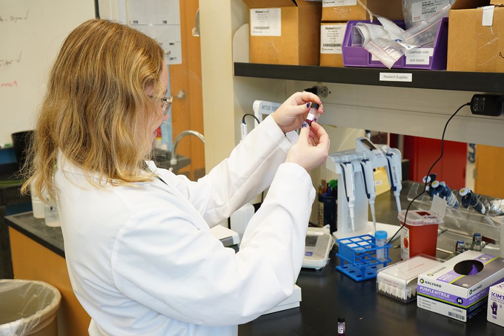 A student looking at a vile of liquid while in a research laboratory.